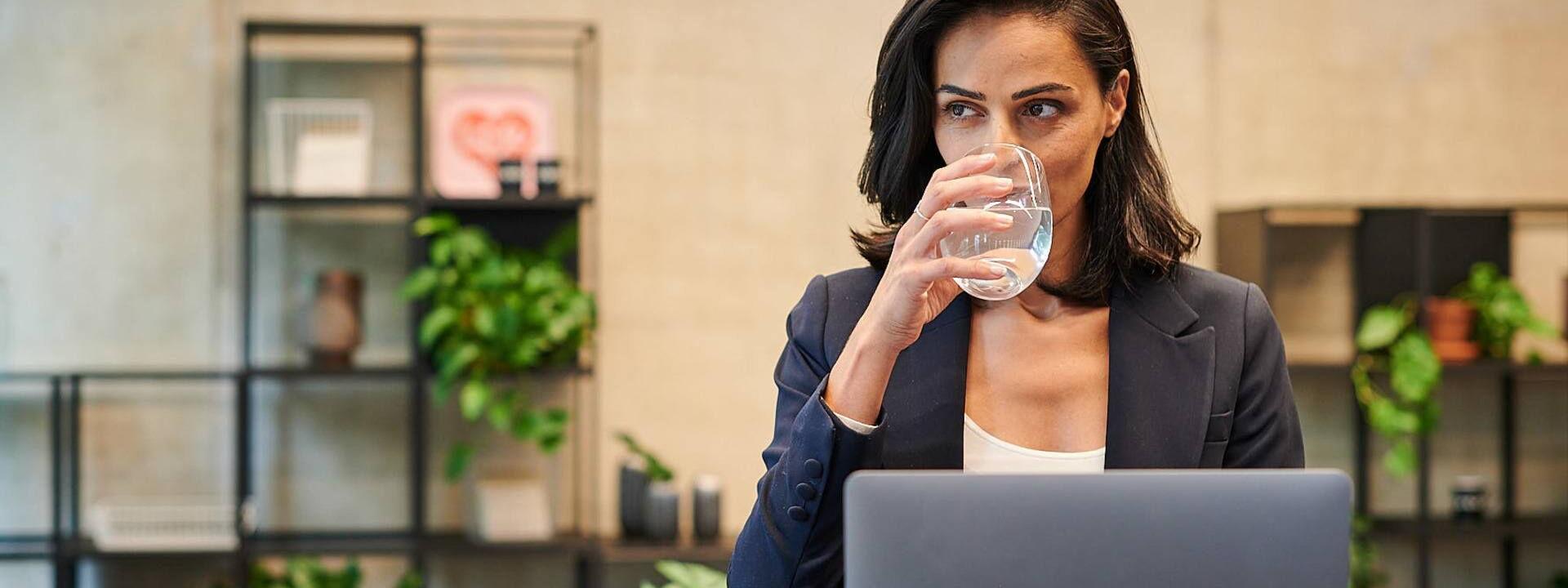 Kollegin trinkt Wasser vor ihrem PC